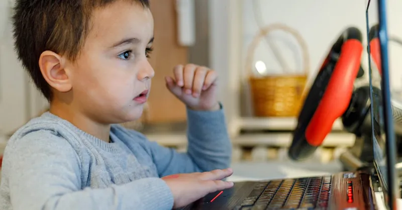 A young child focuses intensely on a laptop screen while learning from home, showcasing modern education.