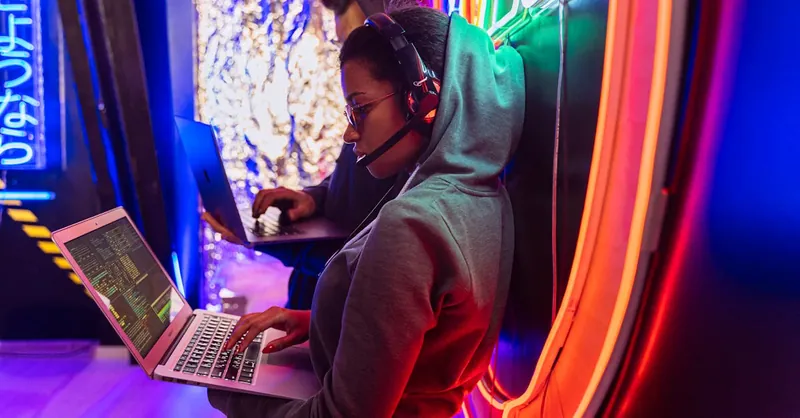 Team of cyber security experts working on laptops in a vibrant neon-lit room.
