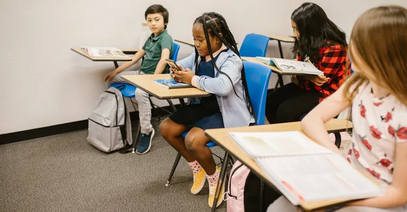 A diverse group of children in a classroom, focusing on social interactions and technology use.