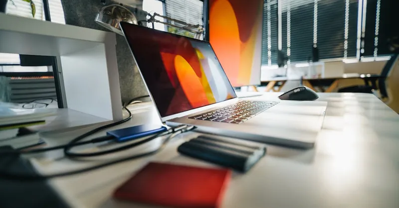 A modern workspace featuring a laptop, external drives, and office equipment on a desk.