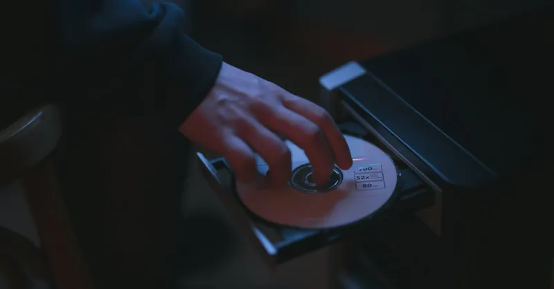 A hand inserting a CD into a computer drive, highlighting cyber security themes.