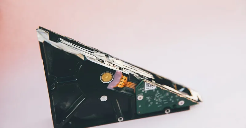 Close-up of a broken hard disk drive showing internal components on a pink background.