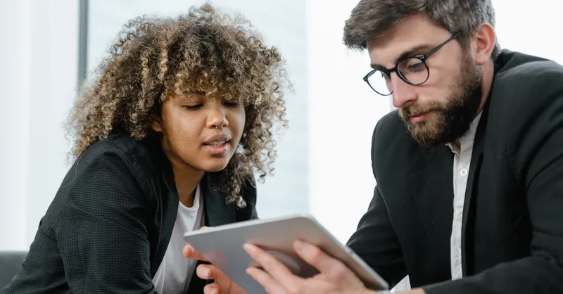 Two business professionals reviewing data on a tablet, fostering collaboration and teamwork in a modern office setting.