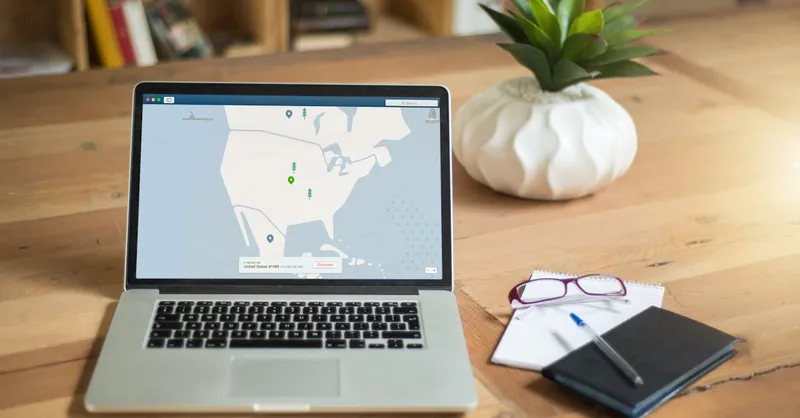 A laptop displaying VPN software sits on a wooden desk with a notepad and plant offering a secure workspace vibe.