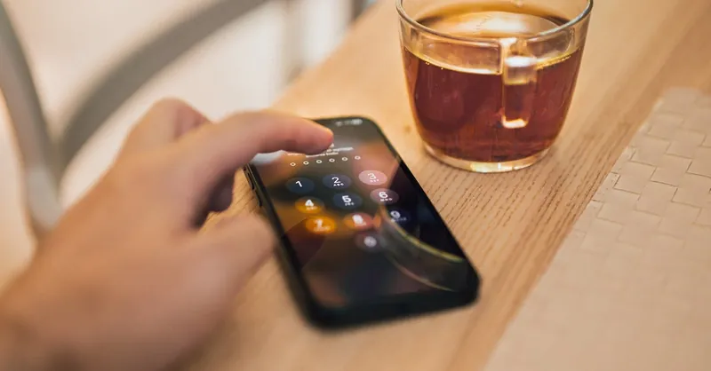 Close-up of hand unlocking a smartphone next to a cup of tea on a wooden table, emphasizing technology and security.
